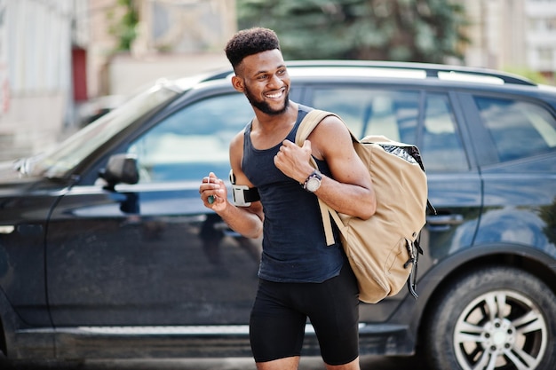 Atleta afroamericano hombre deportivo con mochila contra su auto todoterreno negro antes de entrenar