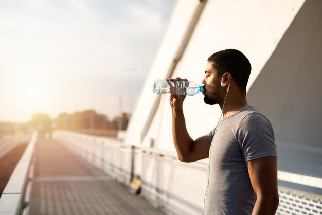Atleta atractivo sosteniendo una botella de agua y bebiendo antes del entrenamiento