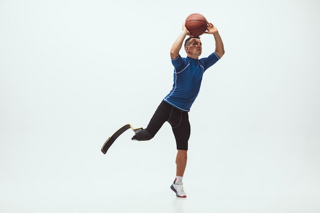Atleta con discapacidad o amputado aislado en el espacio de estudio blanco. Jugador de baloncesto profesional masculino con prótesis de pierna entrenando y practicando en estudio.