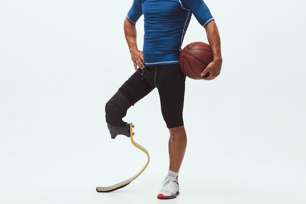 Atleta con discapacidad o amputado aislado en el espacio de estudio blanco. Jugador de baloncesto profesional masculino con prótesis de pierna entrenando y practicando en estudio.