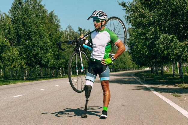 Atleta con discapacidad o amputado entrenando en ciclismo en un día soleado de verano. Deportista masculino profesional con prótesis de pierna practicando al aire libre. Deporte para discapacitados y concepto de estilo de vida saludable.