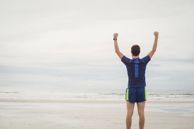 Atleta feliz de pie en la playa con las manos levantadas