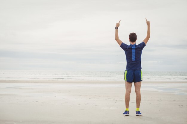 Atleta feliz de pie en la playa con las manos levantadas