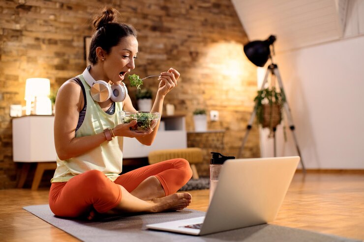 Foto gratuito atleta femenina comiendo ensalada y usando una laptop después de hacer ejercicio en casa