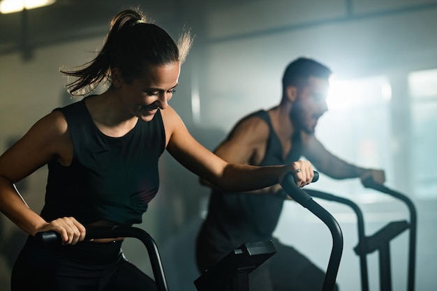 Foto gratuita atleta femenina feliz ciclismo en bicicleta de ejercicio durante el entrenamiento cruzado en el club de salud