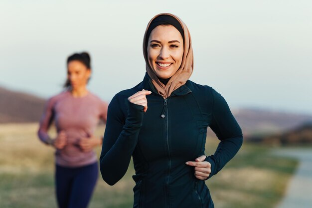 Atleta femenina feliz trotando por la mañana en la naturaleza Su entrenador personal está en el fondo