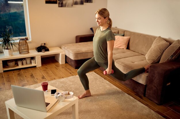 Atleta femenina feliz usando pesas de mano mientras hace ejercicio en casa
