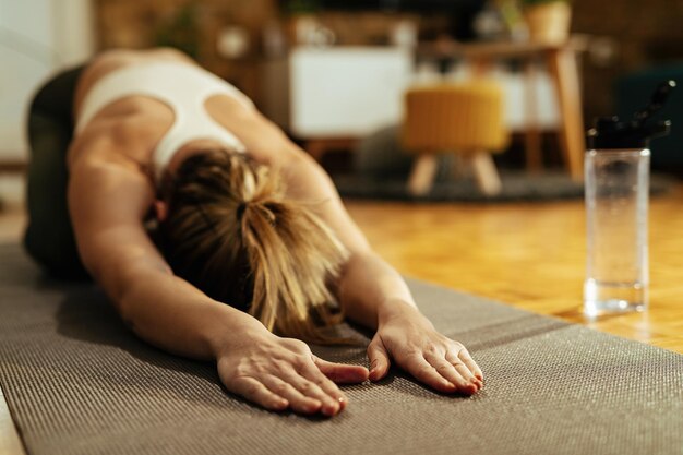 Atleta femenina haciendo ejercicios de relajación y estiramientos después del entrenamiento deportivo en casa.