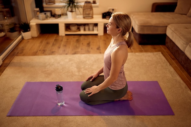 Atleta femenina meditando mientras practica Yoga en la sala de estar