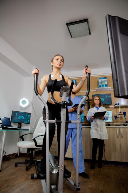 Atleta femenina que hace un esfuerzo físico en el paso a paso y tiene electrodos y médicos pegados en su tableta y en la pantalla de su evolución. Ensayos clinicos