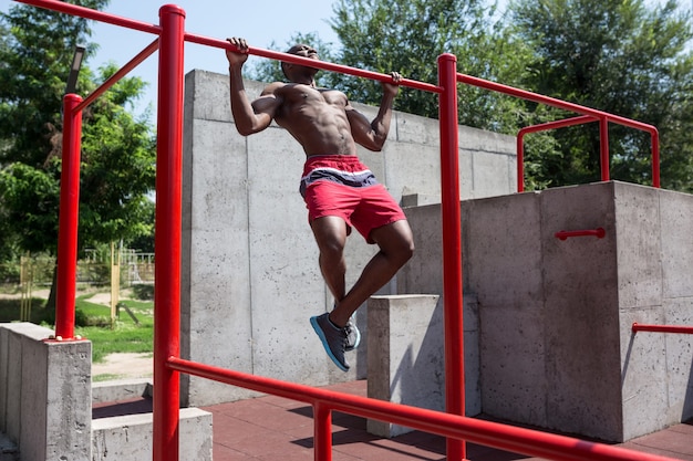 El atleta en forma haciendo ejercicios en el estadio. Hombre afroamericano o afroamericano al aire libre en la ciudad. Tire hacia arriba de los ejercicios deportivos. fitness, salud, concepto de estilo de vida