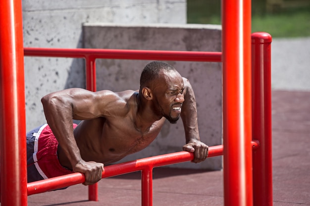 El atleta en forma haciendo ejercicios en el estadio. Hombre afroamericano o afroamericano al aire libre en la ciudad. Tire hacia arriba de los ejercicios deportivos. fitness, salud, concepto de estilo de vida