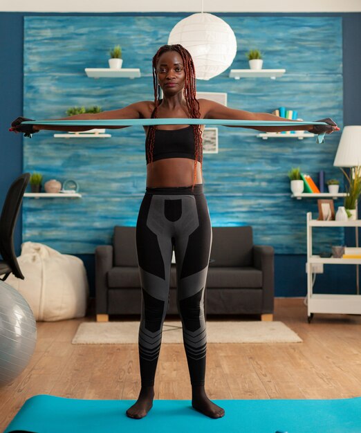 Atleta haciendo ejercicios en casa en la sala de estar con goma elástica en la estera de yoga para los músculos de la espalda