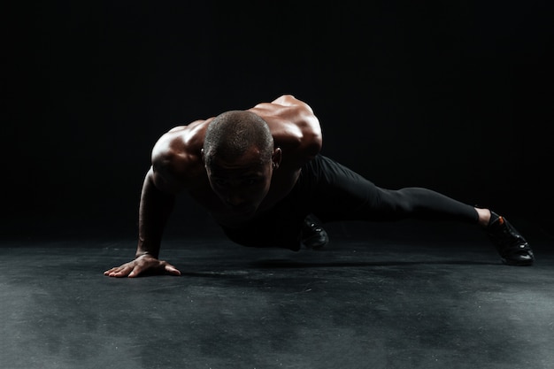 Atleta masculino afroamericano con hermoso cuerpo musculoso haciendo flexiones con una mano en el piso