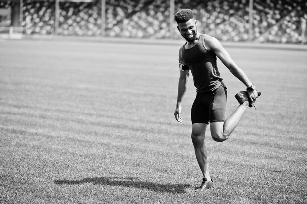 Atleta masculino afroamericano en ropa deportiva haciendo ejercicio de estiramiento en el estadio