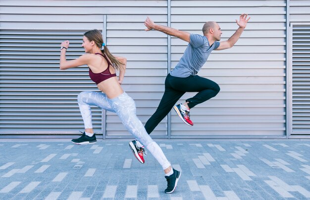 Atleta masculino y femenino joven deportivo activo que corre y que salta en aire