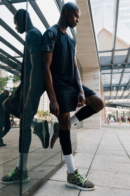 Atleta masculino joven africano contemplado que se inclina en el espejo reflexivo en el aire libre