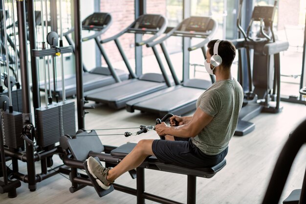 Atleta masculino con mascarilla protectora haciendo ejercicio en una máquina de remo en un gimnasio