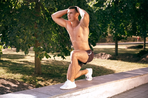 Foto gratuita un atleta masculino musculoso haciendo ejercicio en el parque. gimnasia, entrenamiento, entrenamiento físico, flexibilidad.