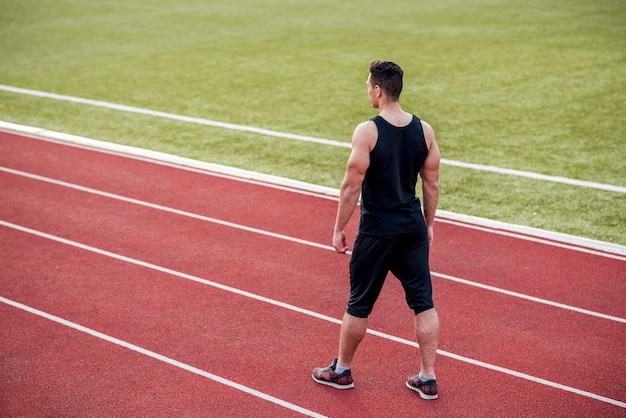 Un atleta masculino de pie en la pista roja en el estadio