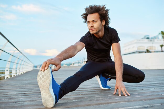 Atleta masculino de piel oscura con cabello tupido haciendo ejercicio y estirando las piernas.