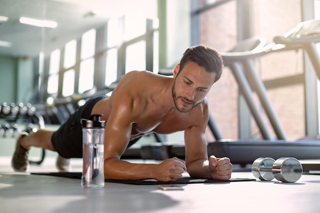 Atleta masculino en pose de tablón ejerciendo fuerza durante el entrenamiento deportivo en un gimnasio