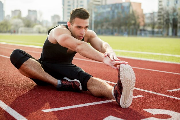 Un atleta masculino que se extiende en la pista de carreras