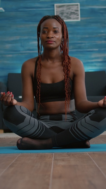 Atleta mujer delgada en posición de loto en el mapa de yoga durante el entrenamiento de fitness matutino en la sala de estar disfrutando de un estilo de vida saludable