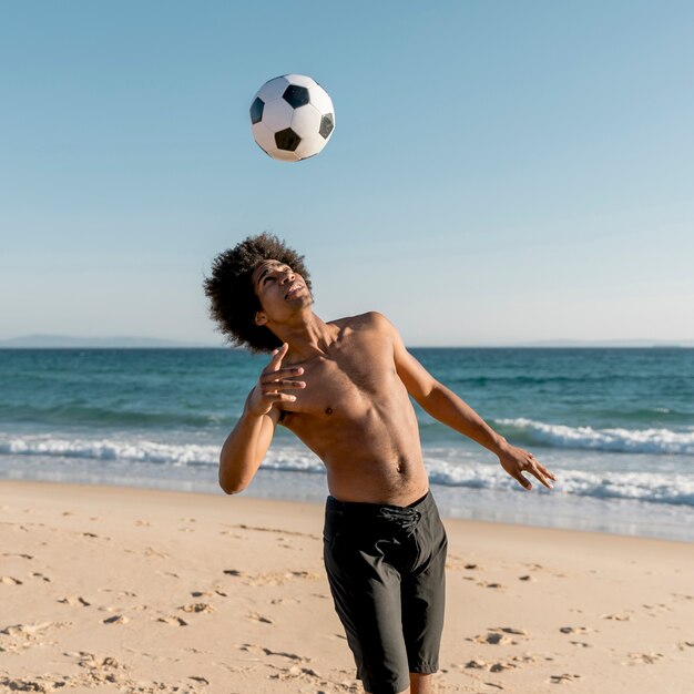 Atleta negro joven que juega el balón de fútbol en la playa