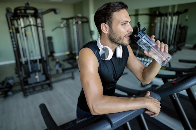 Atleta sediento bebiendo agua después de correr en cinta rodante en el club de salud