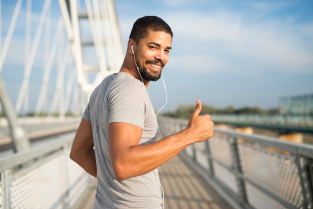 Atleta sonriente con auriculares sosteniendo Thumbs up listo para entrenar