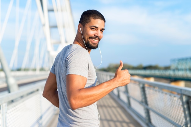 Atleta sonriente con auriculares sosteniendo Thumbs up listo para entrenar