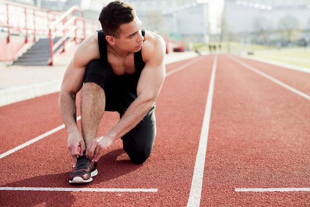 Atleta sprinter preparándose para atar atar los cordones de los zapatos en las pistas de atletismo del estadio