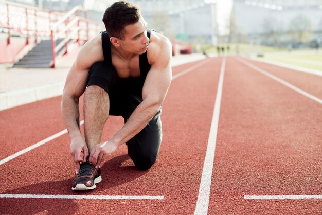 Atleta sprinter preparándose para atar atar los cordones de los zapatos en las pistas de atletismo del estadio