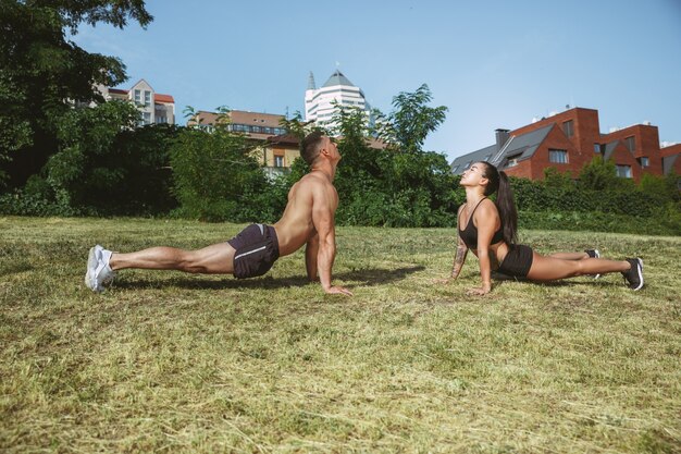 A atletas musculosos haciendo ejercicio en el parque. Gimnasia, entrenamiento, entrenamiento físico, flexibilidad. Ciudad de verano en un día soleado en el campo espacial