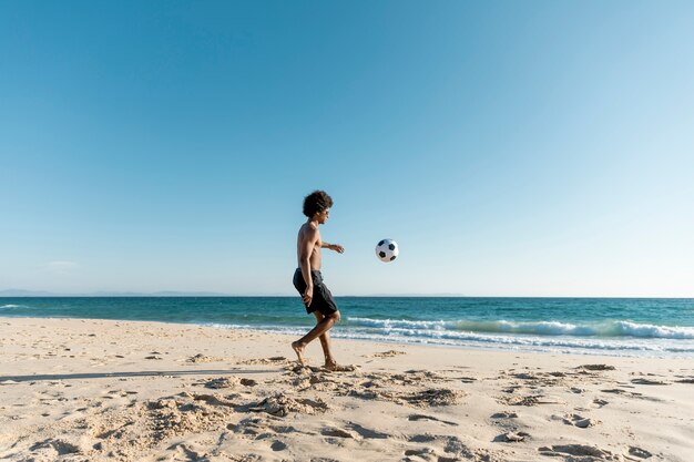 Atlético hombre pateando la pelota en la playa
