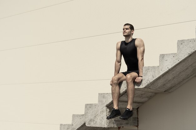 Atlético hombre sentado en las escaleras de hormigón ascendentes