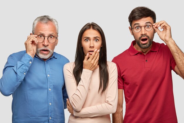 atónito hermano, hermana y su anciano padre posando contra la pared blanca