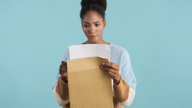 Atractiva chica afroamericana informal que abre un sobre con los resultados de los exámenes sobre un fondo colorido