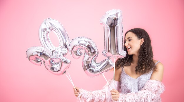 Atractiva chica alegre sobre un fondo rosa con globos plateados para el año nuevo en sus manos