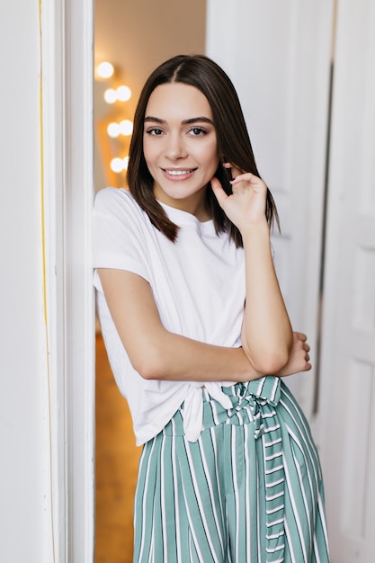 Atractiva chica blanca con peinado recto posando en casa. sonriente mujer magnífica en camiseta.