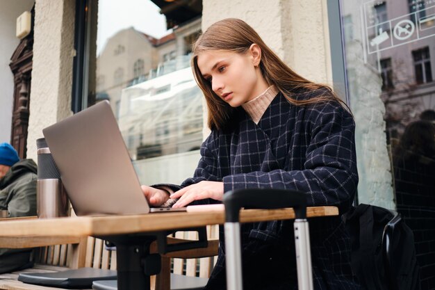 Atractiva chica casual buscando cuidadosamente un lugar para quedarse en la computadora portátil en el café de la calle