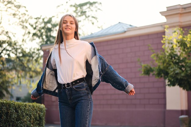 Atractiva chica casual con estilo despreocupada en chaqueta de mezclilla mirando soñadoramente en la cámara al aire libre