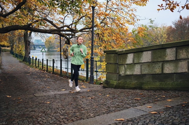 Atractiva chica deportiva corriendo soñadoramente en el acogedor parque de la ciudad de otoño