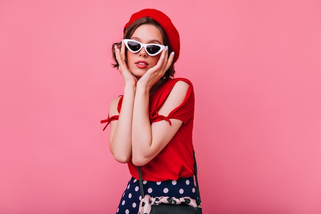 Atractiva chica francesa con piel pálida posando. Foto interior de adorable señorita con gafas de sol de pie.