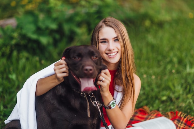 Atractiva chica joven smilling junto con su perro labrador marrón