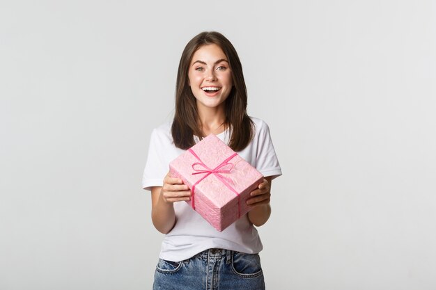 Atractiva chica morena feliz con regalo de cumpleaños y sonriendo alegre.