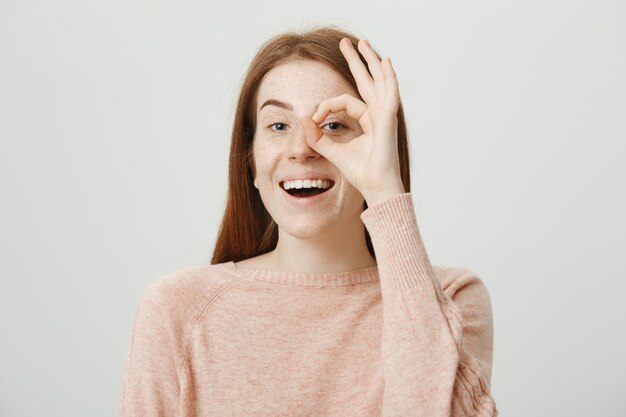 Atractiva chica pelirroja linda mostrando gesto bien sobre el ojo, dar aprobación