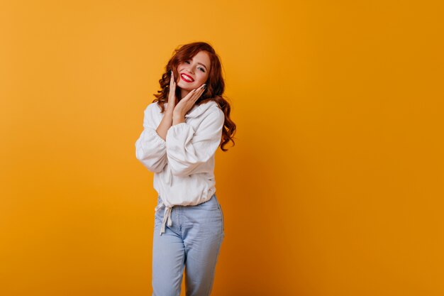 Atractiva chica de pelo largo posando con linda sonrisa. Agraciada señorita blanca de pie sobre la pared amarilla.