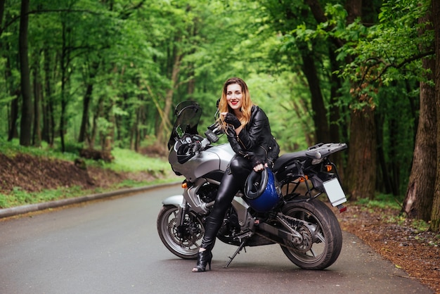 Una atractiva chica sexy vestida de cuero posando cerca de una motocicleta deportiva afuera